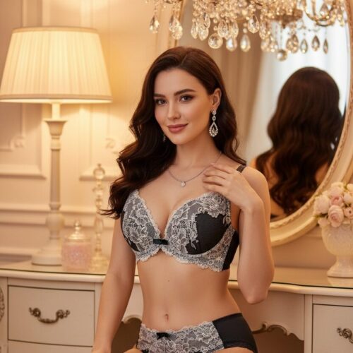 Woman wearing black and grey lace bra and panty set, seated at vanity mirror